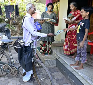 എച്ച് കെ ദാമോദരൻ  സെെക്കിളിലെത്തി  വീടുകളിൽ പുസ്തകം നൽകുന്നു
