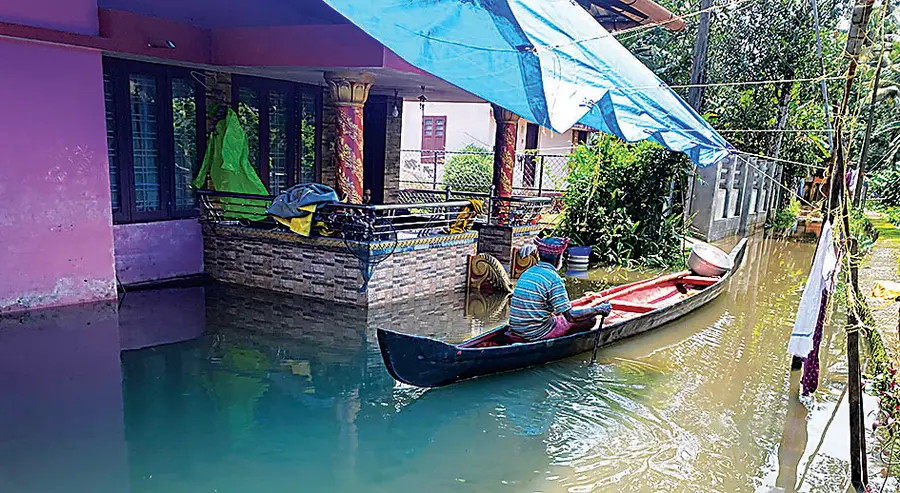 A man in a boat passes in front of a flooded house in Talavadi.