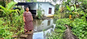 വെള്ളം കെട്ടി നിൽക്കുന്ന വീടിന് മുന്നിൽ പ്രിയ മുരുകേശൻ  